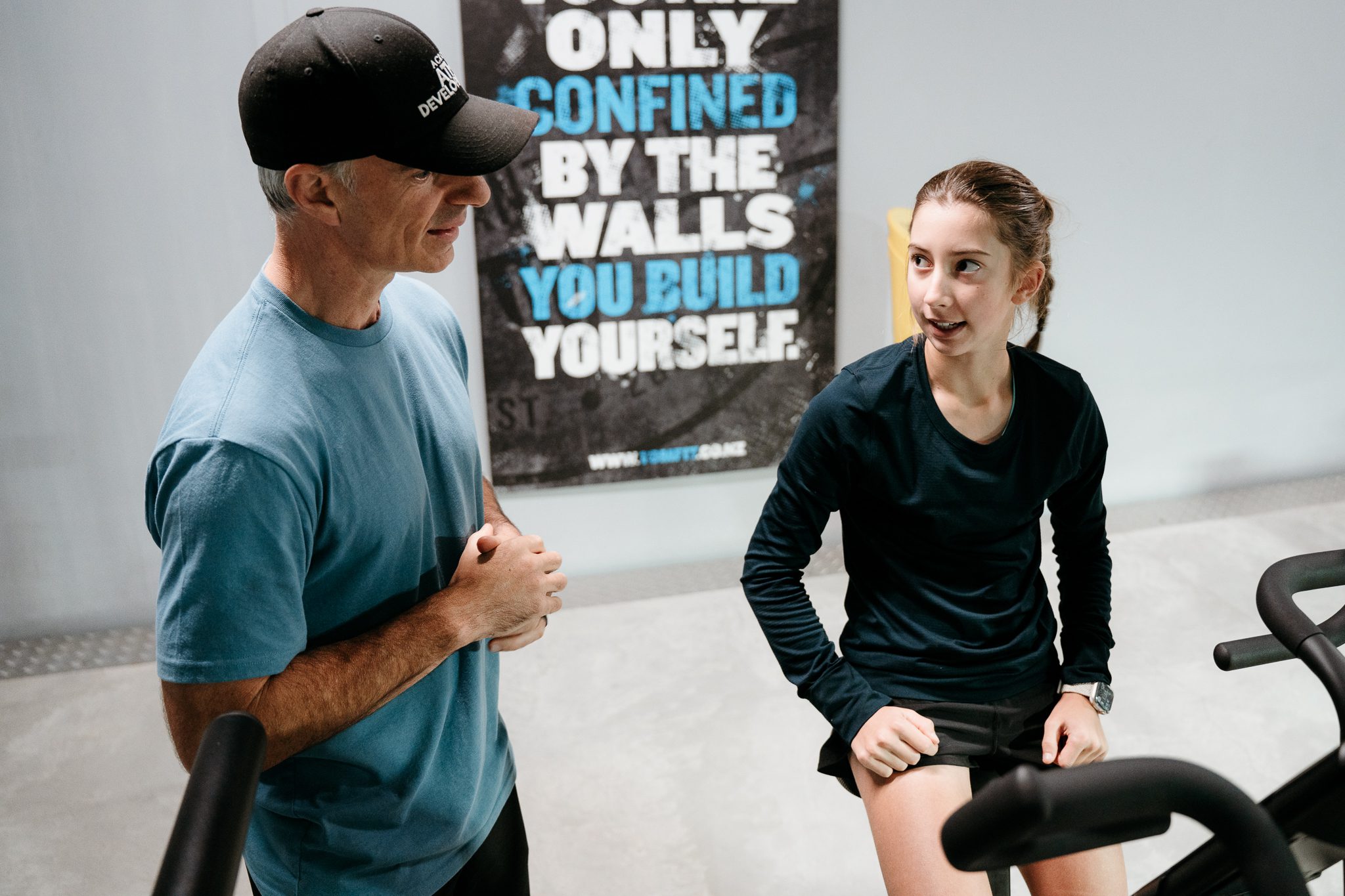 Auckland personal trainer coaching a young athlete during a fitness session at a gym, motivational quote on wall, Auckland group fitness class